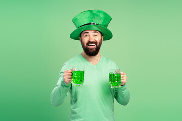 Bearded man wearing leprechaun hat holding two green beers for St. Patrick's Day
