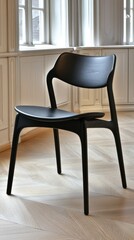 A sleek modern black wooden chair is positioned in a stylish interior room, where expansive windows provide an abundance of natural light
