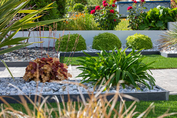 Beau jardin paysag&eacute; fleuri et ses plantes et palmiers au pied d'une habitation au printemps.