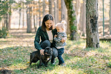 Mom hugs a little girl with one hand, squatting stroking the dog with the second