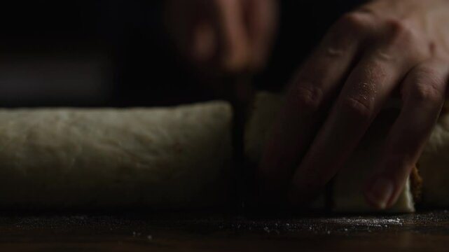 Cinnamon Roll Making: Slicing the dough log into pieces with a knife.