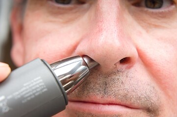 close up of a man using a nose trimmer