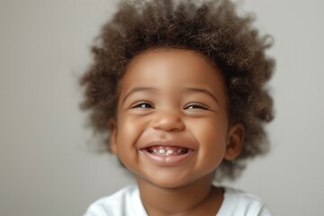 A joyful toddler of African descent with curly hair smiles brightly, showcasing their playful spirit and infectious happiness.