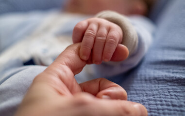 Newborn holding parent's finger with hand