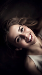 Woman with long brown hair is smiling and has her mouth open. She is wearing a white tank top and is laying down