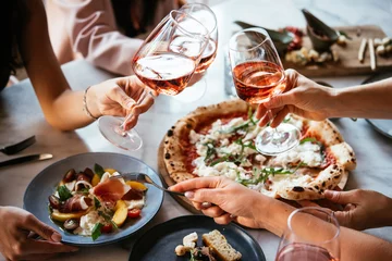 Fotobehang Kruidenier Friends enjoy a dinner party with pizza and rose wine in a bar or a restaurant.  © FornStudio