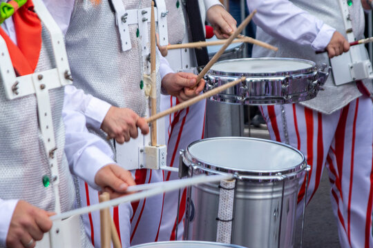 Members of a comparsa play the batucada while advancing in the Tenerife carnival parade, dressed in a white costume with red stripes.