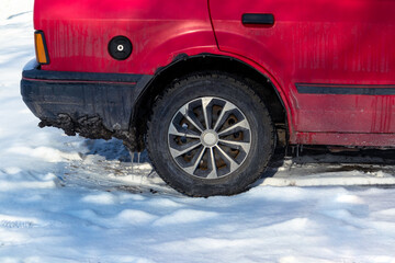 The rear wheel of an old red car on a snowy road