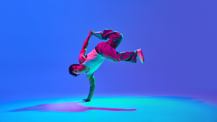 Burst of energy. Talented young guy, contemp dancer in motion, performing against gradient blue...
