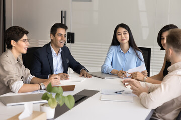 Business negotiations. Group of diverse multicultural businesspeople stakeholders colleagues listen to young man speaking sharing idea at brainstorm session staff meeting conference at boardroom table