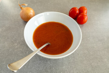 Homemade tomato soup in a white bowl with fresh tomatoes and onion.