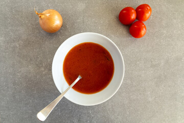 Homemade tomato soup in a white bowl with fresh tomatoes and onion.