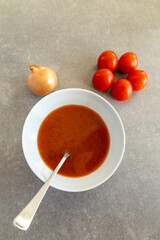 Homemade tomato soup in a white bowl with fresh tomatoes and onion.