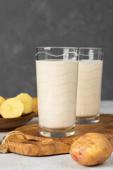 Vegan potato milk in two glass and potato in plate on dark gray background. Plant based milk replacer and lactose free