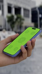 GREEN SCREEN CHROMA KEY Person holding a smartphone with a green screen in an urban setting, surrounded by buildings and people on a cloudy day