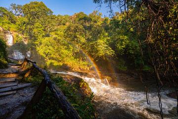 Wachirathan waterfall Chiang Mai is surrounded by lush greenery, with a vibrant rainbow forming in...