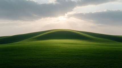 Fototapeta premium Rolling hills of green grass under a sky partially covered in clouds. The sun breaks through casting light rays across the serene scene.