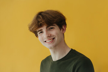 Smiling Young Man in Green Shirt Against a Yellow Background by Studio