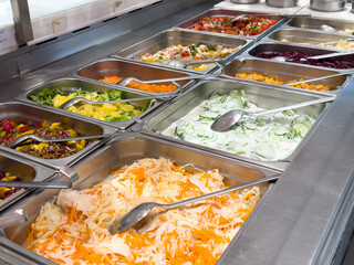 Diverse salad bar with fresh vegetables and toppings in metal trays