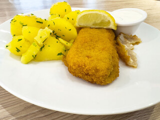 Delicious breaded fish fillet with lemon and herb potatoes on white plate