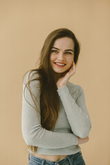 Obraz premium Smiling Woman Posing in Casual Outfit Against Minimalistic Beige Background