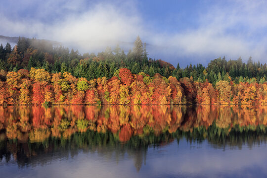 Picturesque Autumn Scene at Loch Faskally, Pitlochry, Perthshire, Scotland, Featuring Rich Fall Colors, Evergreen Forests, and a Stunning Water Reflection with Mist Rolling Over Distant Hills