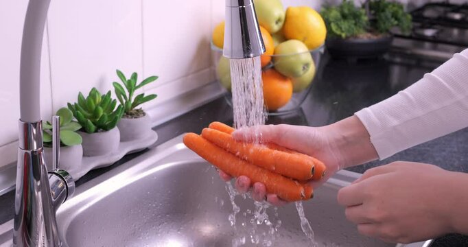 Woman hands washing fresh carrots in the kitchen. Eating healthy raw organic food, vitamins, washing vegetables from pesticides concept. Slow motion 4k