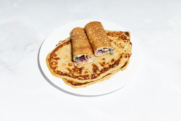 Close-up of a stack of homemade crepes with two rolled ones on top, filled with greens and purple sprouts.