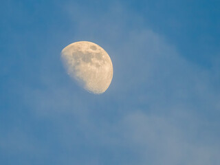 Sunlit yellow moon in blue sky in the daytime, white clouds