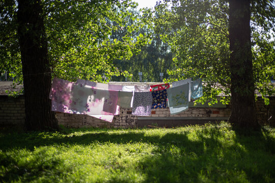 A row of freshly washed laundry hangs on a clothesline outdoors, gently swaying in the breeze. The bright sunlight casts soft shadows on the ground, while the wind helps the fabric dry naturally. 