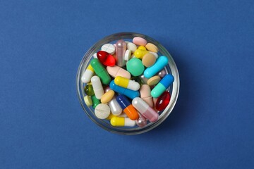 Bowl with pills on blue background, top view