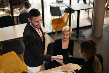 In a stylish café setting, a young businessman hands his business card to a female client, fostering professional networking and engagement.
