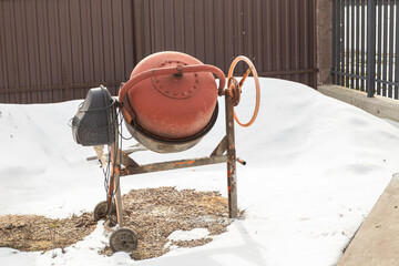 Concrete mixer. Machine for making concrete. Snow around. Stone, gravel and sand nearby. Close-up