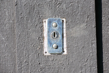 Rectangular metal keyhole plate labeled UP with two screws is mounted on a garage wooden door. Emergency release lock plate with a keyhole and two screws