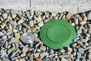Green pop-up drainage emitter installed on a pebble-covered surface, accompanied by a circular...