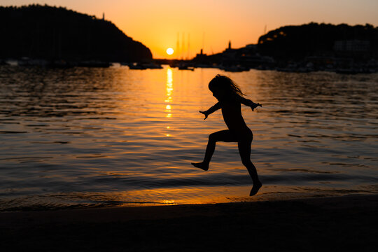 Silhouette of a child playing by the water at sunset in Soller