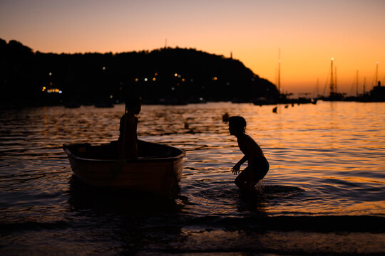 Children playing by the boat at sunset near a tranquil shore in Soller