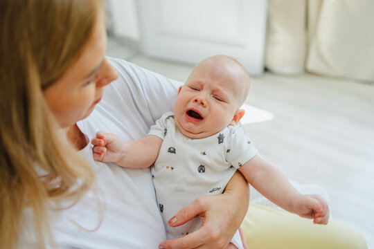 Mother comforting a crying baby in bright living room