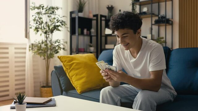 Happy teen boy counting dollars, saving for a dream, personal finance goals
