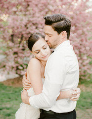 Fototapeta premium Couple embraces amidst blooming cherry blossom trees during a romantic outdoor wedding in spring
