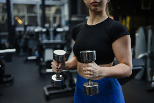 Focused blonde woman lifting dumbbells in modern gym setting