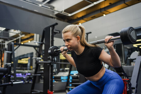 Focused blonde woman performing squat exercise in modern gym