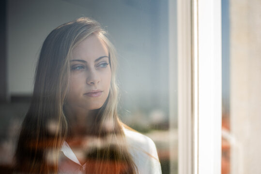 Pensive woman gazing through window with soft reflections