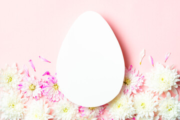 White egg-shaped card on a pink background. Surrounded by delicate white and pink flowers. A beautiful concept for Easter.