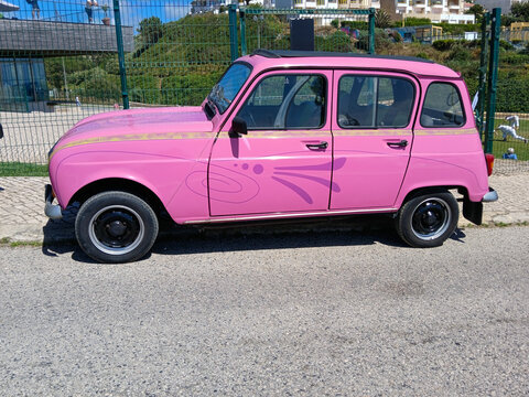 Pink renault 4l parked near a fence with decorative swirls on its side