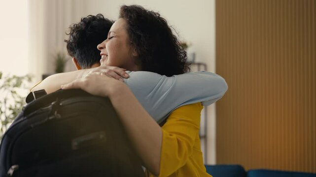 Happy middle-aged woman embracing her adolescent son returning home from college