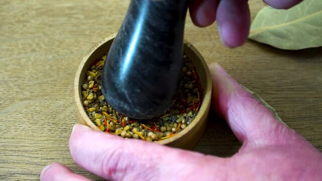 Hand Grinding Spices in Wooden Bowl. Mixture of aromatic spices: coriander seeds, basil, dill, bay leaf, saffron, fenugreek.