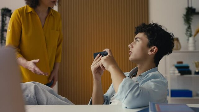 Teenage son playing on his phone, ignoring his annoyed mother, family conflict