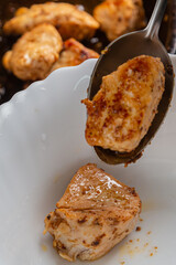 Chicken pieces fried in a frying pan with sauce and spices are transferred