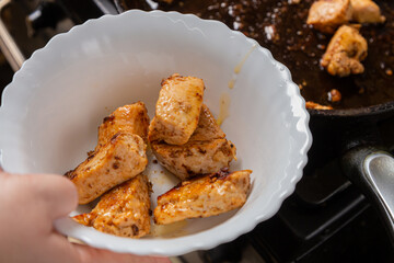 Chicken pieces fried in a frying pan with sauce and spices are transferred from the frying